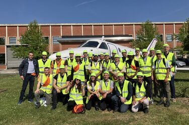 Eine Gruppe von Menschen steht und kniet vor einem Flugzeug.