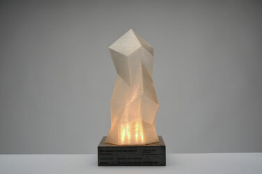 Award developed by students for the digital methods in architecture course, consisting of a square, dark concrete base and a 3D-printed, crystalline structure above it with lighting switched on