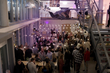 Many guests celebrate in the festively lit foyer of the faculty with several floors and fairy lights. The atmosphere is lively and sociable.