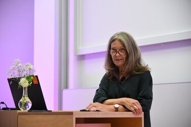 Dean Diana Reichle leans against the lectern on the stage and welcomes the audience.