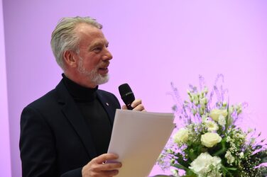 Prof. Helmut Hachul stands on stage with a microphone and congratulates the students on their award.