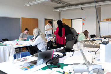 Blick in den Arbeitsraum mit Studierenden und Lehrenden der Summerschool mit Arbeitsmodellen und Kubaturen auf den Tischen.