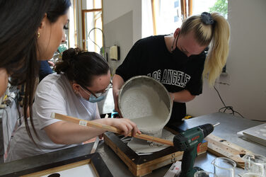 Studentinnen gießen angerührten Beton in eine Holzschalung