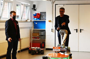 Mayor Thomas Westphal and Daniel Heß stand around OmniMan in IDiAL's robot lab.