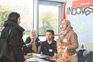 Vier junge Menschen in einem Gespräch an einem internationalen Messestand aus Indonesien beim "Marktplatz der Möglichkeiten"__Four young people in conversation at an international trade fair stand from Indonesia at the "Marketplace of Opportunities"