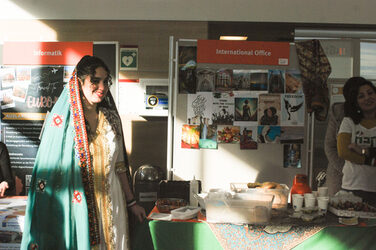 Eine junge Frau steht lächelnd in traditioneller Kleidung vor dem iranischen Länderstand beim internationalen "Marktplatz der Möglichkeiten"__A young woman stands smiling in traditional dress in front of the Iranian country stand at the international "Marketplace of Opportunities"