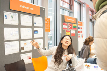 Eine junge Frau stellt einem interessierten Studenten den Messestand der Elektrotechnik vor. A young woman introduces an interested student to the electrical engineering exhibition stand.