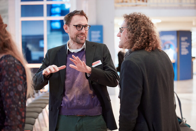 Zwei Mitarbeiter im Gespräch miteinander, einer gestikulierend__Two male employees in conversation, one gesticulating