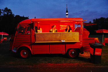 The Citroën HY at the PSD Bank Cinema 2019. The picture shows an evening scene. The HY is illuminated, the side wall is tilted up. Two students stand inside and look out.