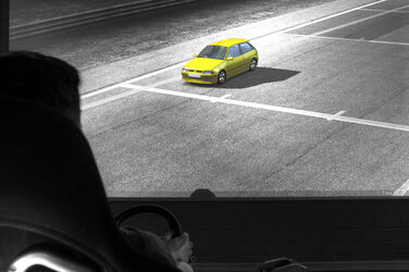 A yellow car can be seen on a large screen. In the foreground, a persona can be seen in silhouette at a steering wheel.