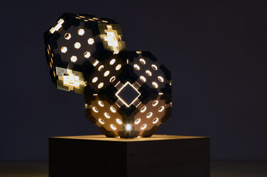 Night shot of an illuminated, sculptural hexagon luminaire on a wooden base with generatively manufactured elements