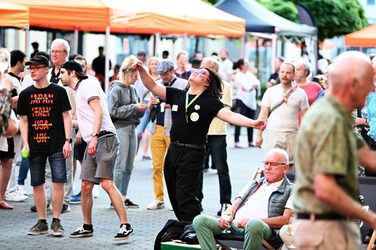 A person in black clothing dances, lost in music, in the midst of many other people.