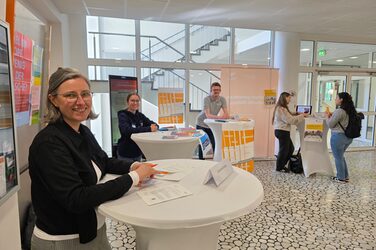 Mehrere Personen stehen an Tischen in einem Foyer.