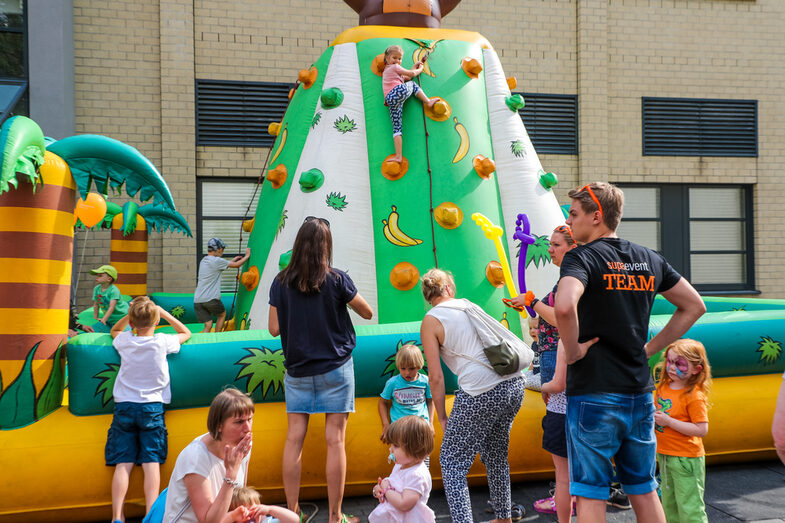 Erwachsene und Kinder stehen vor einer Hüpfburg. Mehrere Kinder befinden sich auf dieser Hüpfburg.