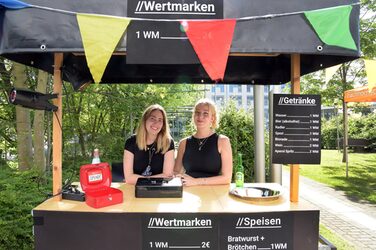 Zwei Teammitglieder der Fachschaft am mit Wimpeln dekorierten Stand zum Wertmarkenverkauf.