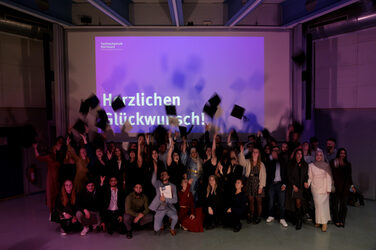 The graduates throw their graduation hats in the air, while "Congratulations!" appears on the screen in the background. The scene celebrates the graduation in a festive mood.