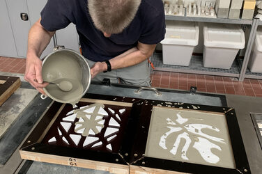 Mann mit Eimer voller Beton in der Hand gießt zwei Platten aus