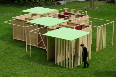 The result of the workshop can be seen from a bird's eye view. A person walks around the structure, which is standing on a meadow.