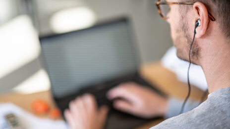 Seitliches Foto eines Mannes mit In-Ear-Kopfhörern im Ohr, der an einem Computer arbeitet.