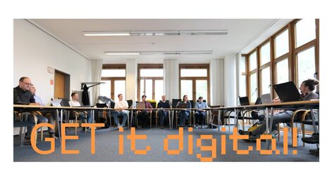Several people take part in a meeting in an open U-shaped table arrangement. Several windows at the back and right of the picture. The access door at the back left. At the bottom of the picture in orange lettering: "GET it digital!"
