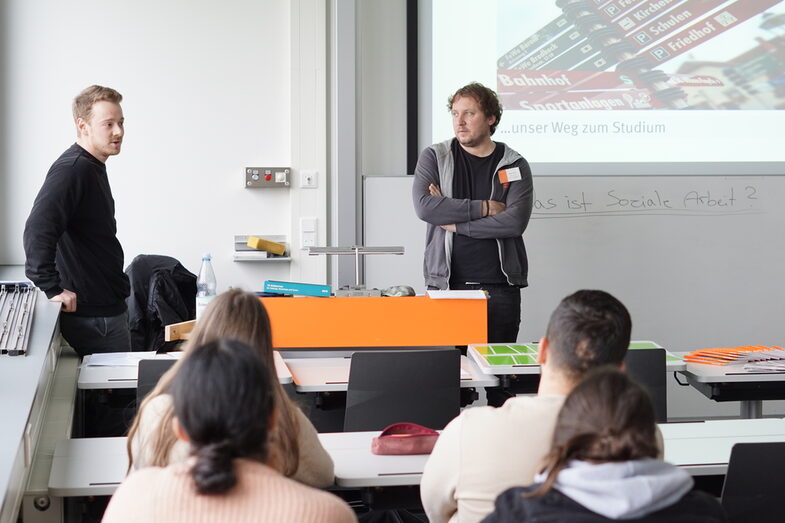 Zwei Studierende stehen vor einer Klasse und halten einen Vortrag beim Schnuppertag Soziale Arbeit.