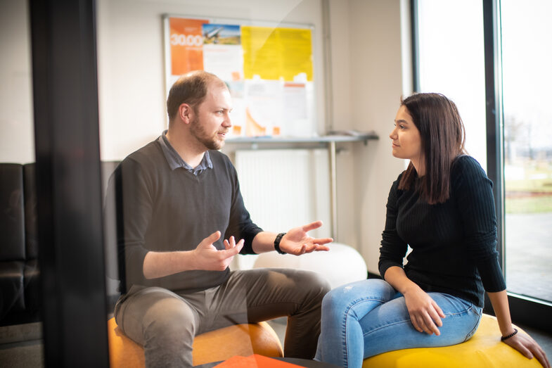 Ein TalentScout und eine Schülerin, die auf Sitzsäcken sitzen und sich unterhalten. Vor ihnen liegen auf einem Beistelltisch einige orangefarbene Mappen.