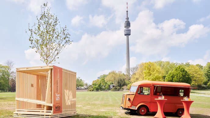 Eine Holzkonstruktion in Würfelform steht auf einer Wiese.