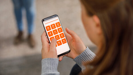 Foto über die Schulter einer Studentin auf ihr Smartphone, die App der Fachhochschule Dortmund ist geöffnet.__Young woman is typing on the smartphone, the app from Fachhochschule Dortmund is open.