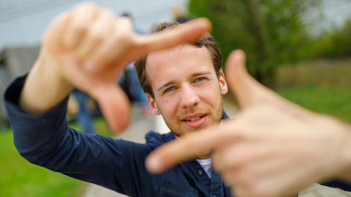 Foto eines Studenten, der mit Zeigefingern und Daumen vor sich ein Quadrat formt und dadurch guckt.