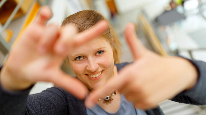 Foto einer Studentin, die mit Zeigefingern und Daumen vor sich ein Quadrat formt und dadurch guckt.
