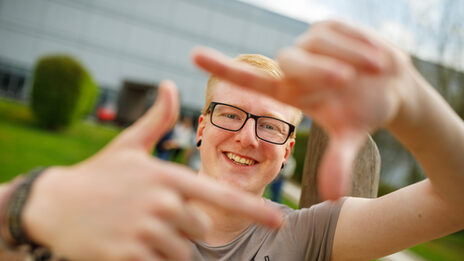 Photo of a student forming a square with his index fingers and thumb in front of him and looking through it.