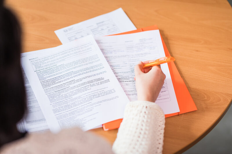 Cropped photo of a person filling out a stack of documents.