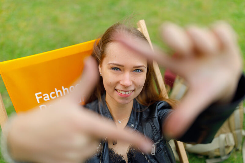 Foto einer Studentin, die mit Zeigefingern und Daumen vor sich ein Quadrat formt und dadurch guckt.