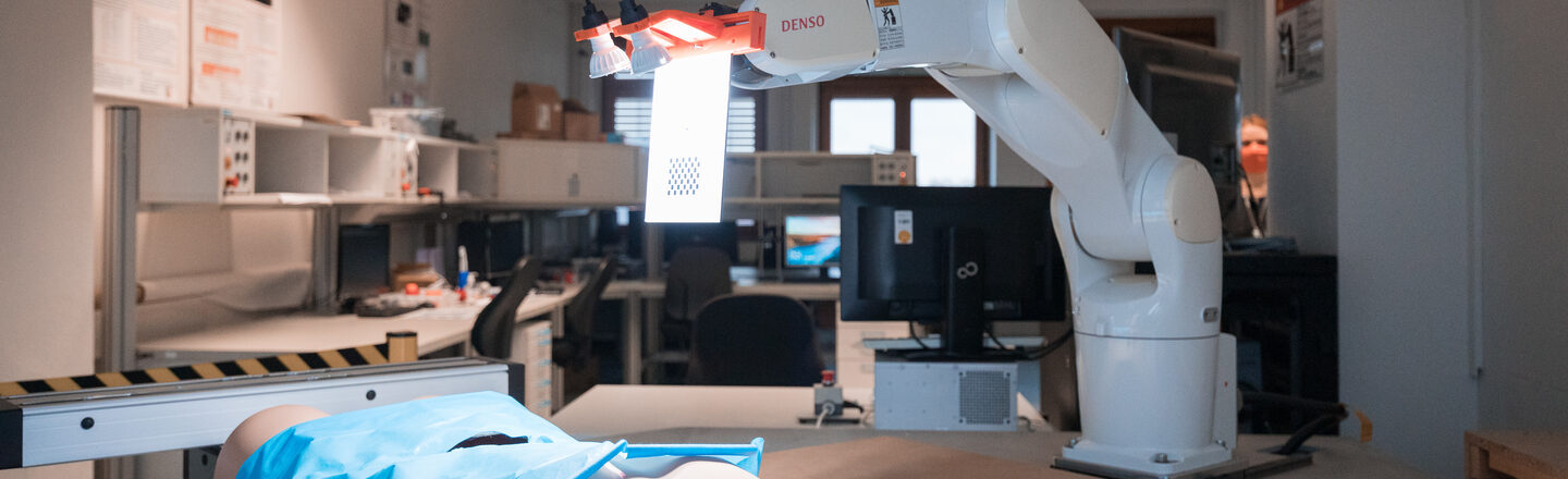 Foto eines OP-Roboters in Aktion. Vor ihm liegt ein künstlicher Torso mit einem blauen OP-Abdecktuch darüber.