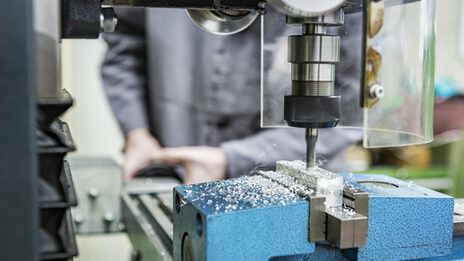 Photo of a person working with a milling machine in the mechanical workshop. The machine is milling something into a piece of metal.