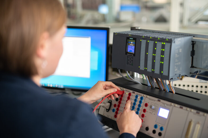 Foto eines Frau im Anschnitt, die ein Kabel in ein Gerät zur Steuerung steckt. Daneben ein PC-Bildschirm.