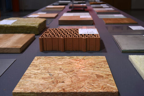 Square samples of different materials made of wood or stone lie on a table. They are provided with small explanatory labels.