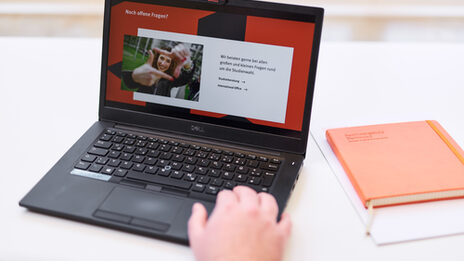 Foto eines Laptops, auf dem die Folie einer Präsentation mit der Überschrift „Noch offene Fragen?“ aufgerufen ist. Die Hand einer Person liegt auf der Tastatur.