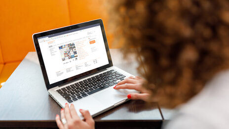 Photo over the shoulder of a female student on a laptop visiting the website of Fachhochschule Dortmund on her laptop __A female student is sitting and visiting the website of Fachhochschule Dortmund on her laptop.