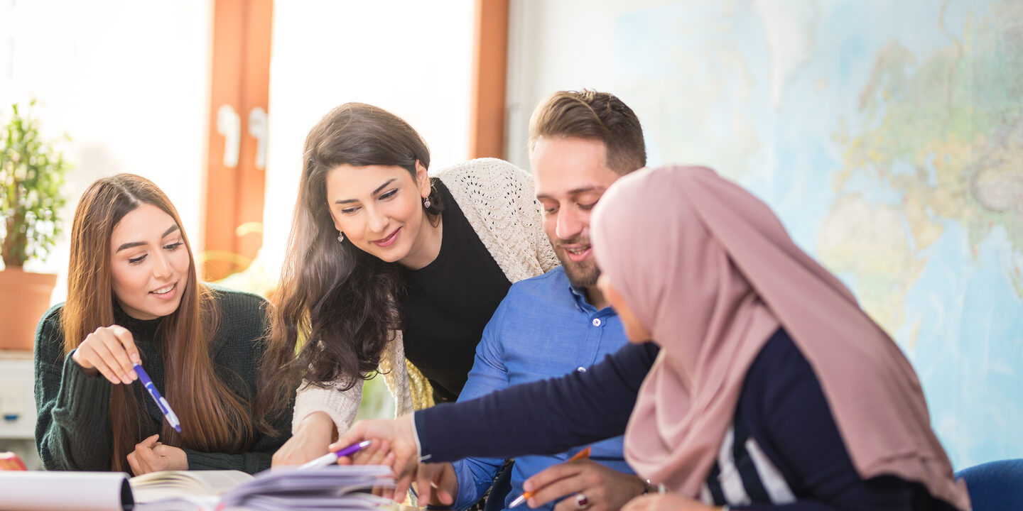 Foto von vier internationalen Studierenden, die gemeinsam Unterlagen diskutieren, die vor ihnen auf einem Tisch liegen.