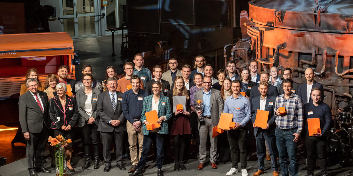 Photo of a group of people. This group is standing on a stage. Some are holding certificates in their hands.