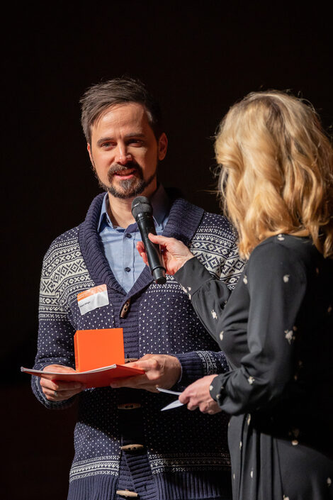 Dr. Robert Höttger accepts his award. He says words into a microphone held by a blonde woman.