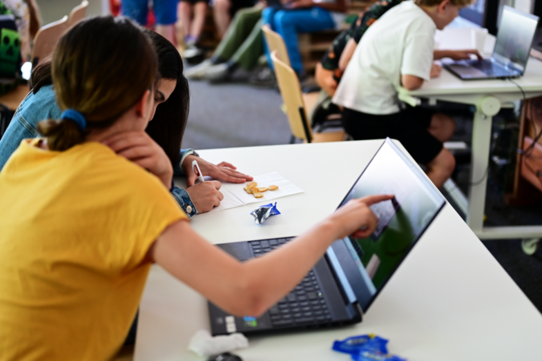 Zwei Schülerinnen sitzen vor einem Notebook und zeichnen einen Algorithmus auf eine Servierte.