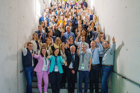 Group photo of the E-TEMS 2025 conference participants standing on the steps of a staircase and raising their thumbs up.