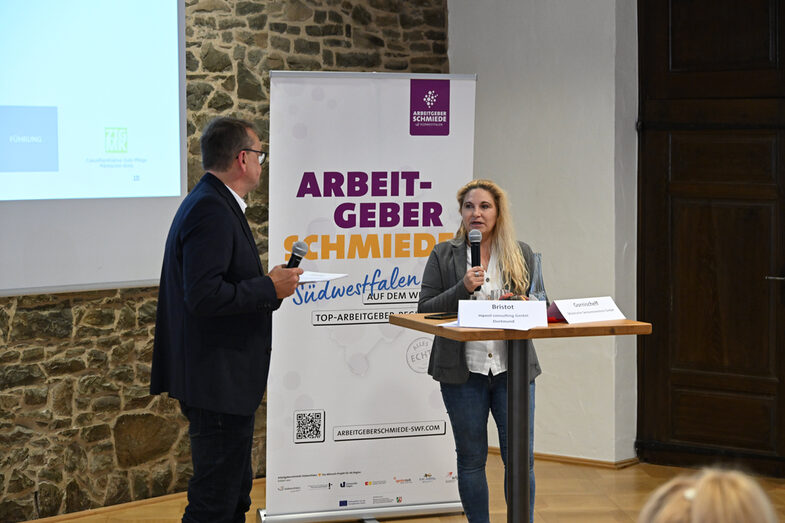Standing at a table, Ansgar Rahmacher, Marcel Mitas and Leon Sachweh present assistance systems for the health and care sector.