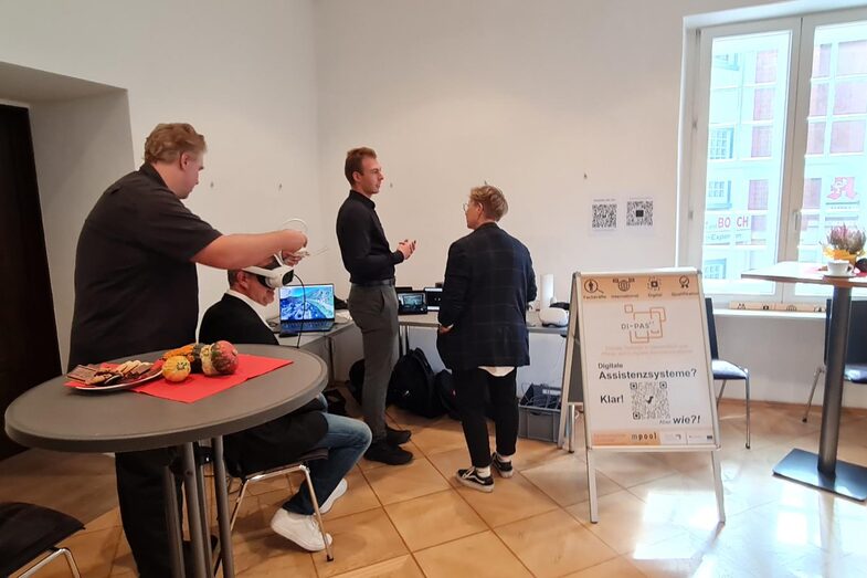 Standing at a table, Ansgar Rahmacher, Marcel Mitas and Leon Sachweh present assistance systems for the health and care sector.
