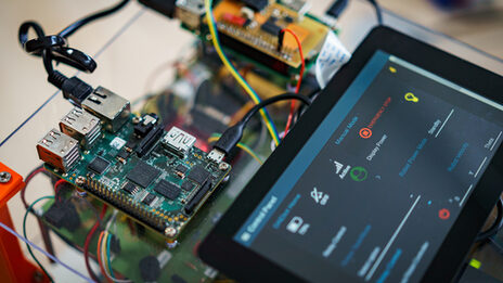 Close-up of a robot assembly with circuit boards and a tablet on which software is open.