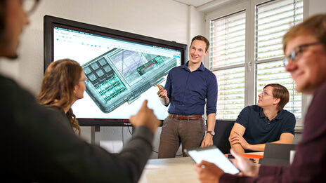 Photo of a meeting situation in which an employee presents something to his colleagues on a screen.