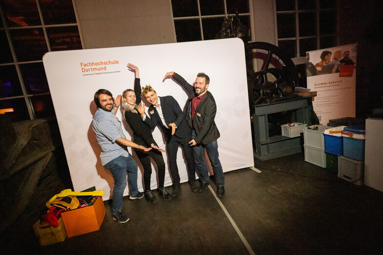 People stand in front of a photo wall with the words "Fachhochschule Dortmund" and pose for the photographer.