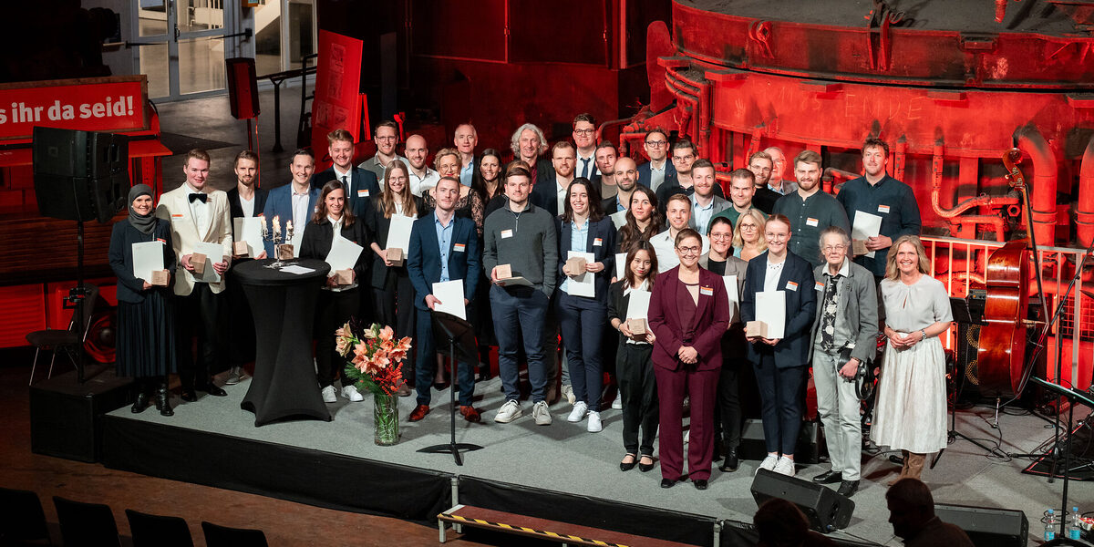 Many people stand on the stage in front of the blast furnace in the DASA steel hall.